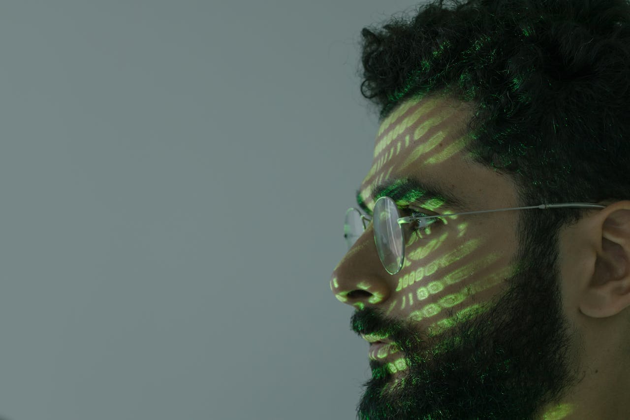 Side profile of a man with eyeglasses and green binary code projected on face.